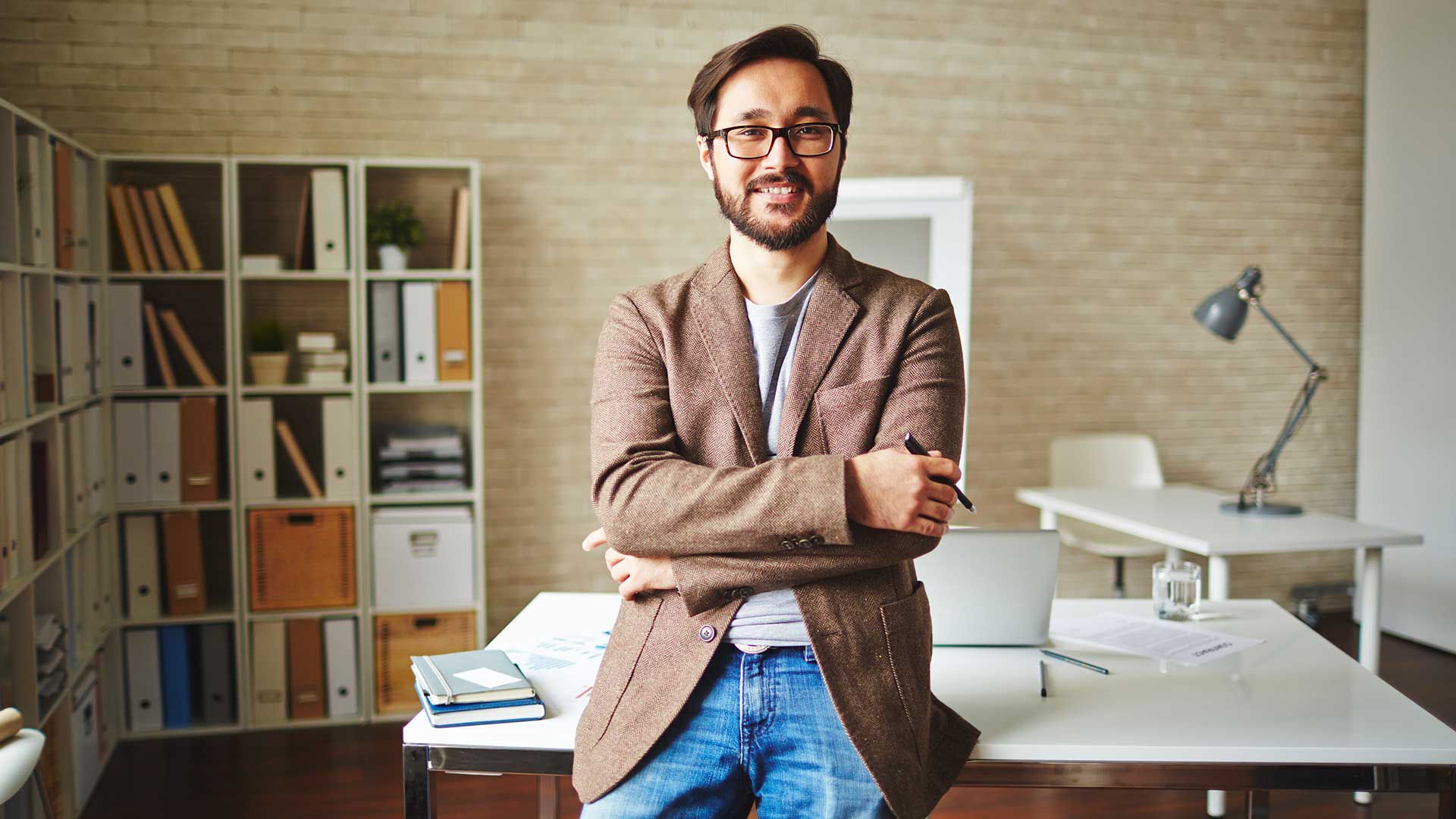 Professional man leaning on desk with a smile and crossed arms